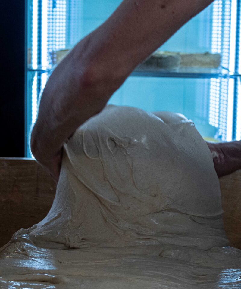 Deux mains façonnent une pâte à pain au levain dans le pétrin
